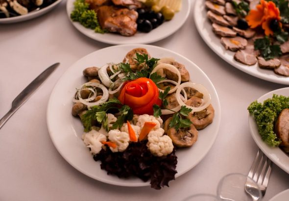 Beautifully arranged gourmet plates with meats, cheeses, and garnishes on a white table setting.