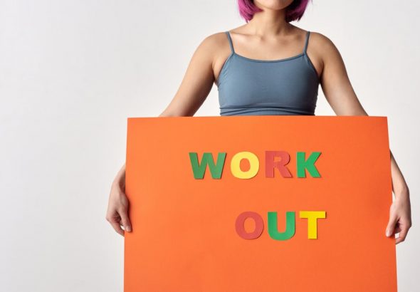 Woman with short hair holding a vibrant 'Work Out' sign on a white background.